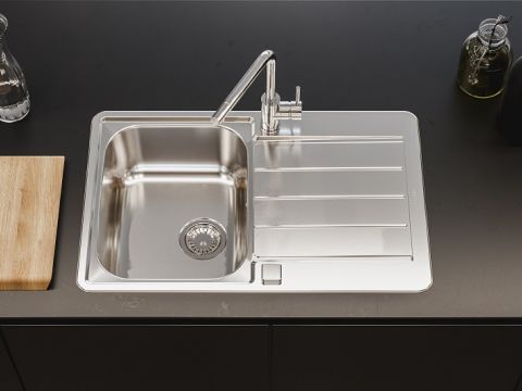 Fregadero de acero inoxidable con escurridor y grifo de cocina cromado sobre una superficie negra