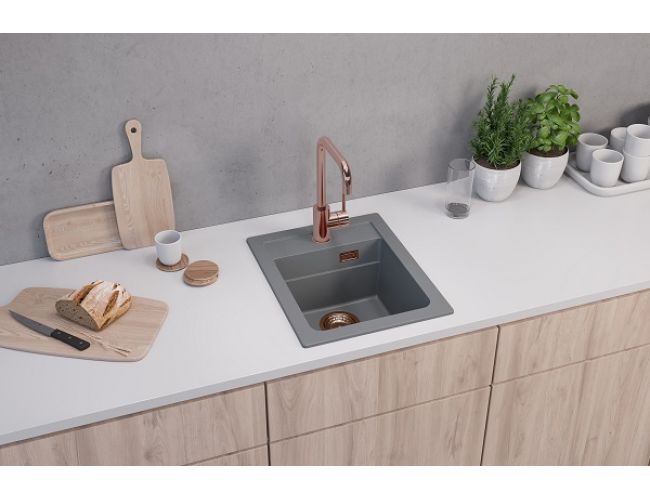 Fregadero de granito gris empotrado en una encimera de cocina blanca, con un grifo de cocina de cobre y un desagüe de cobre