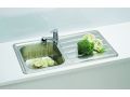 Fregadero de acero inoxidable con escurridor, una lechuga y verduras en él, y brócoli en la superficie de escurrido