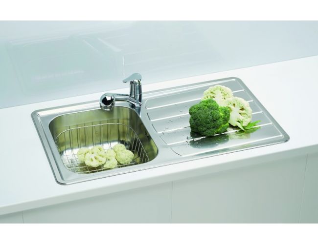 Fregadero de acero inoxidable con escurridor, una lechuga y verduras en él, y brócoli en la superficie de escurrido