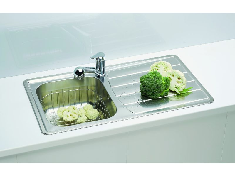 Fregadero de acero inoxidable con escurridor, una lechuga y verduras en él, y brócoli en la superficie de escurrido