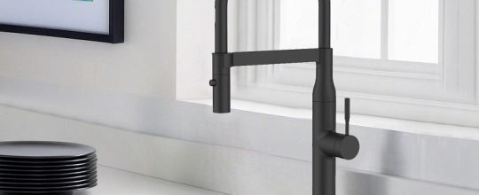Grifo de cocina blanco y fregadero de acero inoxidable en una cocina blanca con un fondo verde o naturaleza visible a través de la ventana