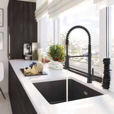 Grifo de cocina profesional ALveus en color negro combinado con un fregadero negro de instalación bajo encimera en una cocina moderna en blanco y negro con grandes ventanales y vistas a la ciudad