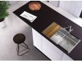 Fregadero Alveus y accesorios: tabla, escurridor AllRound sobre una superficie de trabajo negra en la que también hay un periódico y una bandeja, junto a la cual hay un pequeño taburete de bar