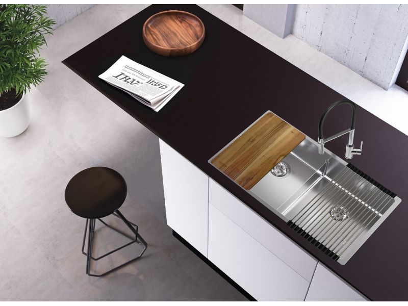 Fregadero Alveus y accesorios: tabla, escurridor AllRound sobre una superficie de trabajo negra en la que también hay un periódico y una bandeja, junto a la cual hay un pequeño taburete de bar