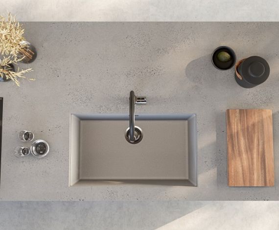 Fregadero de cocina de granito Alveus Omni bajo encimera en color hormigón, instalado en una encimera de cocina del mismo color. Al lado también hay una tabla de cortar