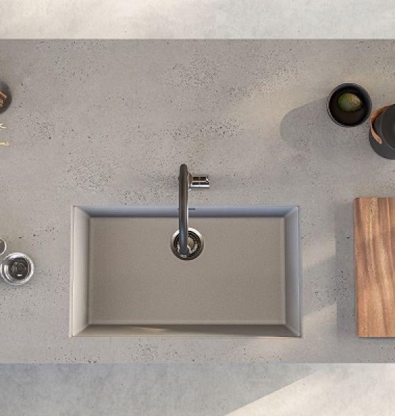 Fregadero de cocina de granito Alveus Omni bajo encimera en color hormigón, instalado en una encimera de cocina del mismo color. Al lado también hay una tabla de cortar