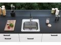 Fregadero de cocina de un seno de acero inoxidable con grifo de cocina negro en una cocina elegante, con una tabla de cortar de madera y especias sobre la encimera