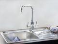 Inox kuhinjsko pomivalno korito z odcejalno površino in visoko kromirano armaturo; na odcejalni površini je skodelica s krožničkom in čajnikom z modrim vzorcem.