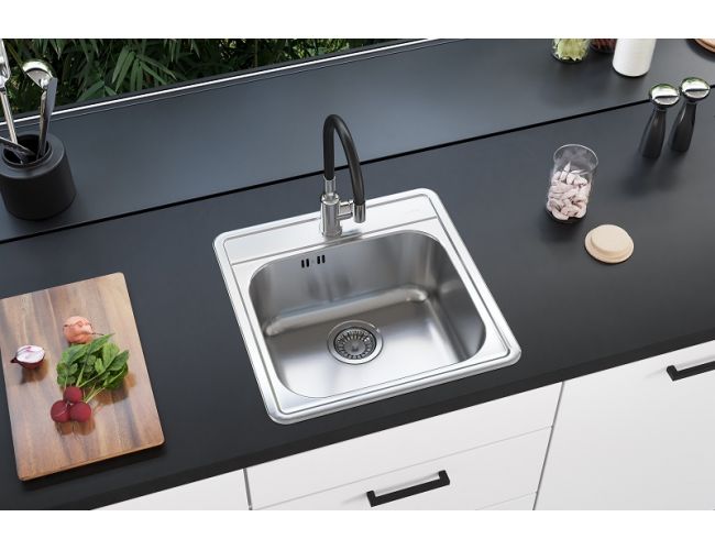Moderno fregadero de cocina de un seno fabricado en acero inoxidable con grifo de cocina negro en una cocina en blanco y negro y una tabla de cortar de madera sobre la encimera