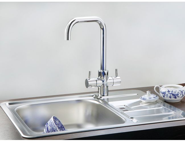 Inox kuhinjsko pomivalno korito z odcejalno površino in visoko kromirano armaturo; na odcejalni površini je skodelica s krožničkom in čajnikom z modrim vzorcem.