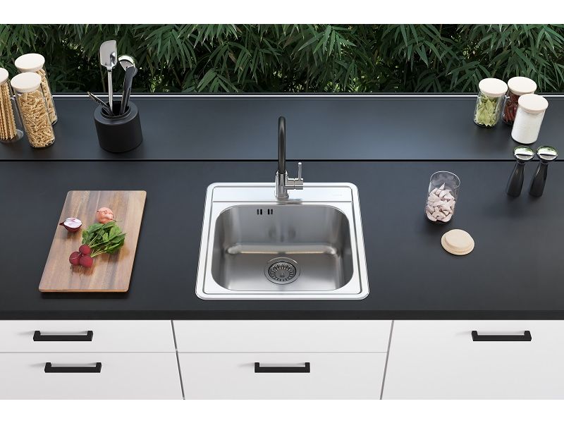 Fregadero de cocina de un seno de acero inoxidable con grifo de cocina negro en una cocina elegante, con una tabla de cortar de madera y especias sobre la encimera