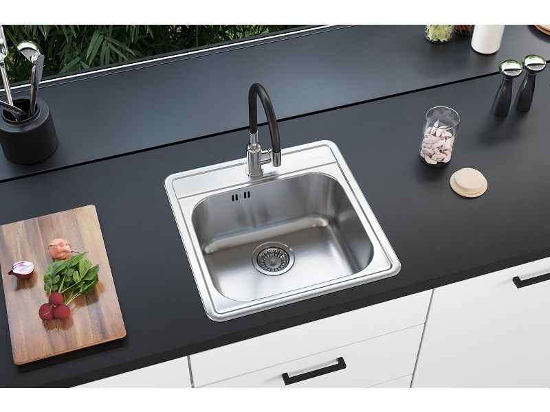 Moderno fregadero de cocina de un seno fabricado en acero inoxidable con grifo de cocina negro en una cocina en blanco y negro y una tabla de cortar de madera sobre la encimera